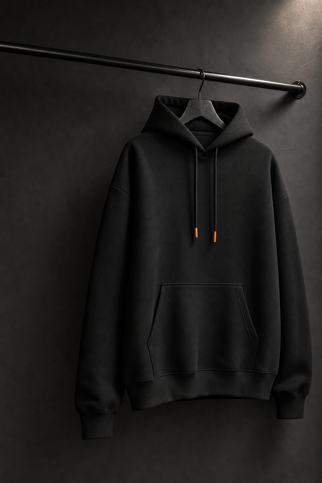 Heavyweight boxy hoodie hanging in a dark studio with orange drawcord tips